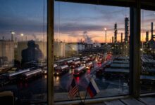 Fleet of tanker trucks at an oil refinery seen through a window with US and Russian flags