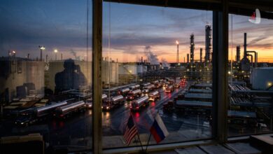 Fleet of tanker trucks at an oil refinery seen through a window with US and Russian flags
