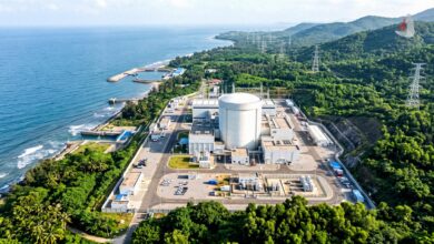 Aerial view of a coastal nuclear power plant facility with a reactor containment dome surrounded by tropical greenery