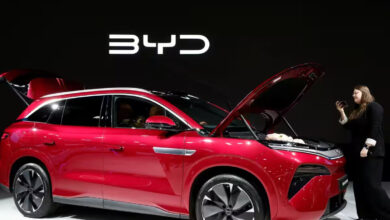 Red BYD electric SUV on display at an auto show with a woman taking a photo