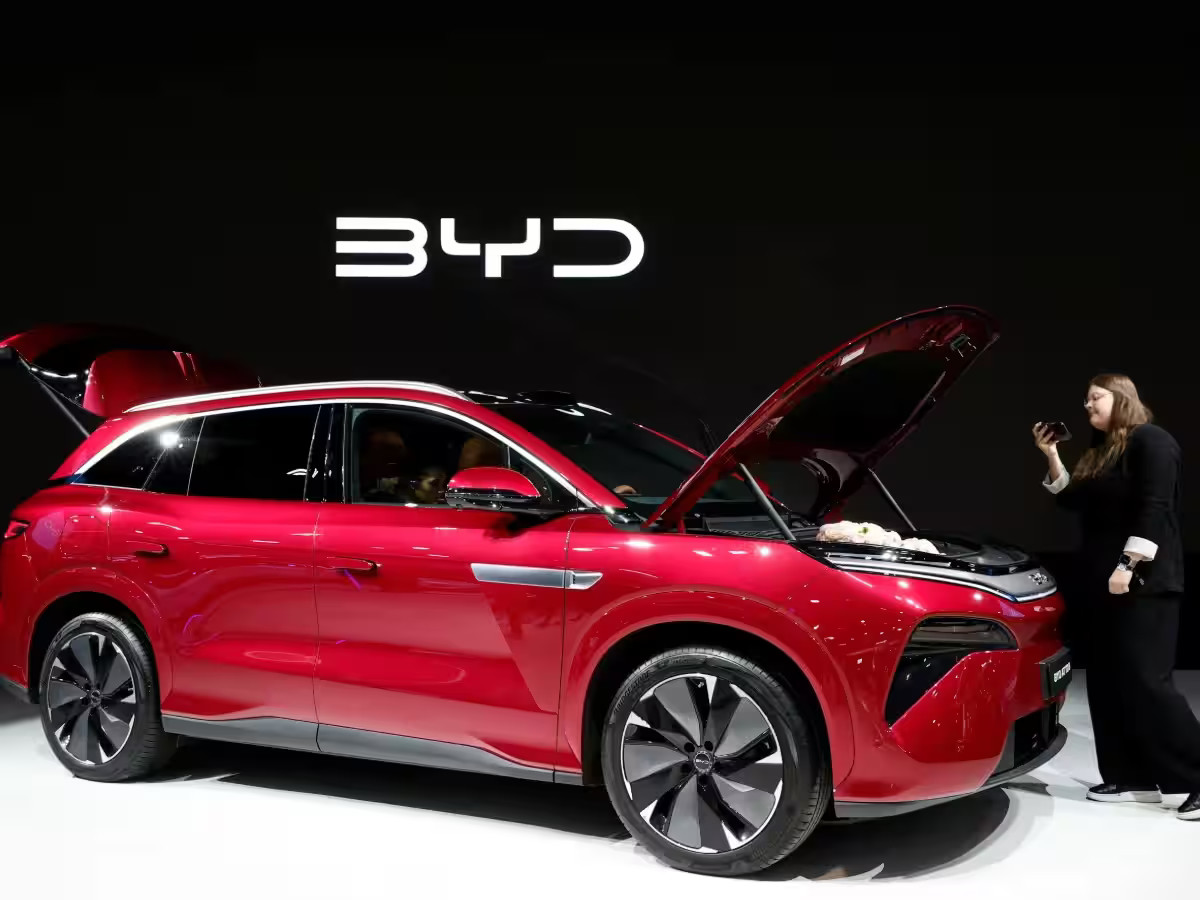 Red BYD electric SUV on display at an auto show with a woman taking a photo