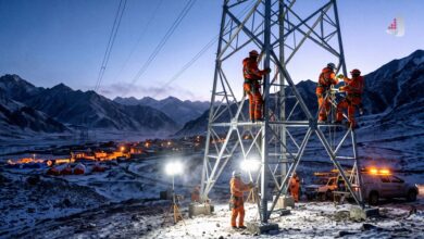 Utility workers repairing a transmission tower in snowy mountains at night