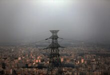 High-voltage power transmission pylon standing against an expansive urban cityscape covered in smog
