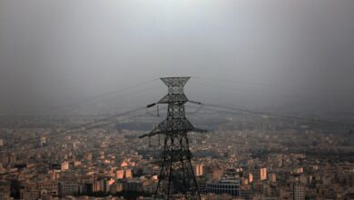 High-voltage power transmission pylon standing against an expansive urban cityscape covered in smog