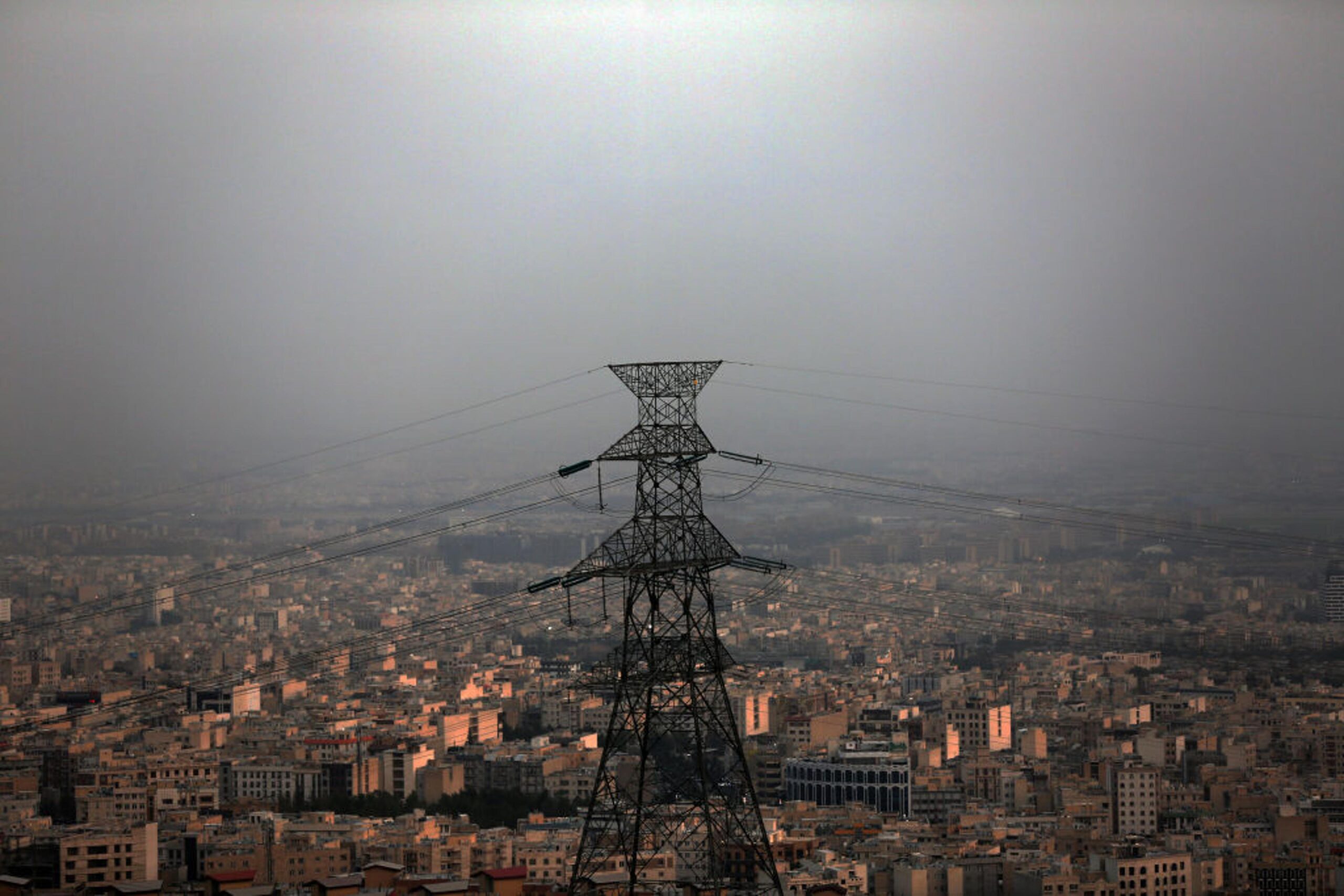 High-voltage power transmission pylon standing against an expansive urban cityscape covered in smog