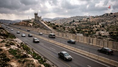 Multi-lane highway with tall concrete barrier walls, a watchtower, and moving vehicles in the West Bank