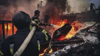 Ukrainian firefighters extinguishing a massive fire amid burning debris and heavy smoke
