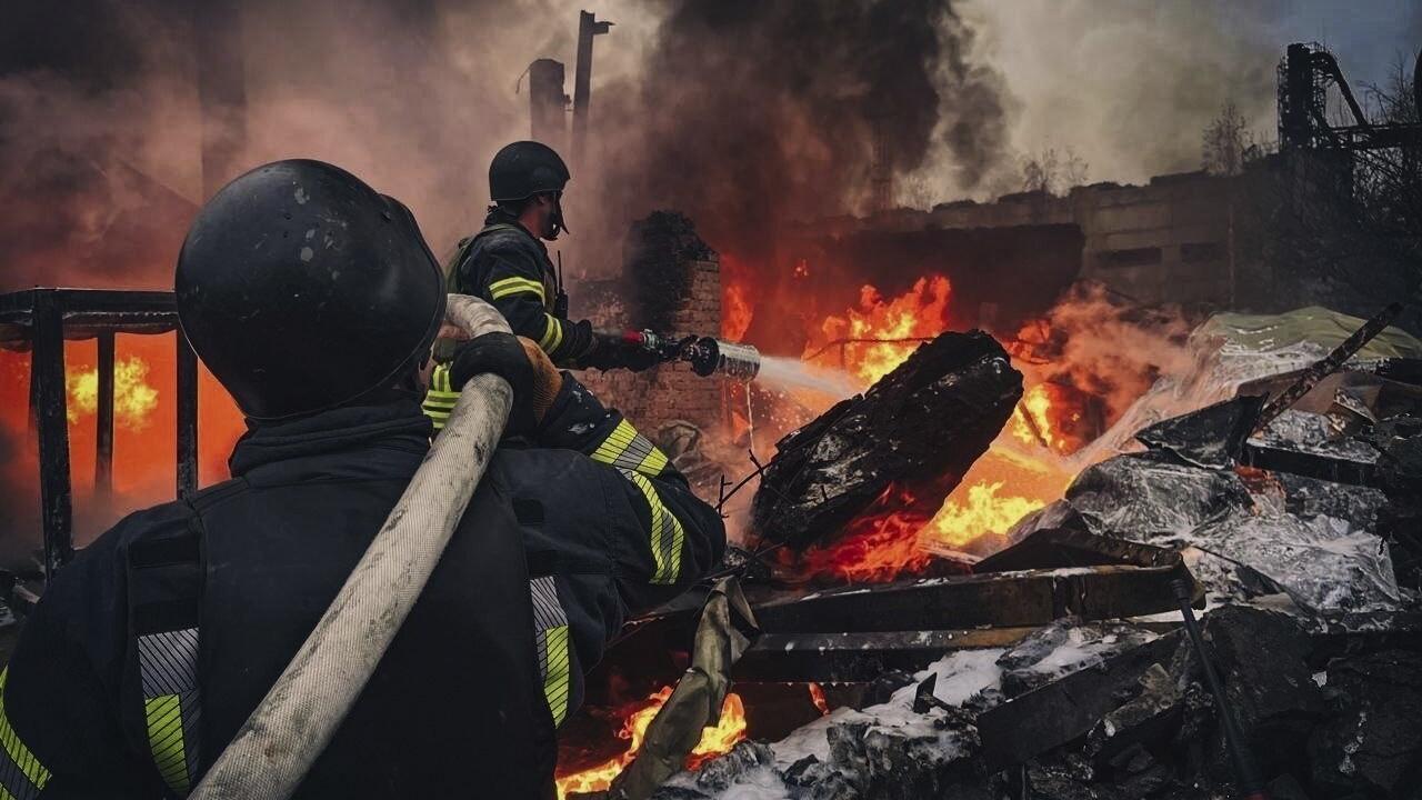 Ukrainian firefighters extinguishing a massive fire amid burning debris and heavy smoke