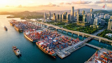 Aerial view of a busy shipping port with cranes and containers near a modern city skyline