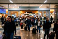 Travelers pulling luggage and waving small Israeli flags while exiting airport terminal doors