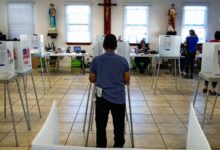 A man fills out a ballot at a polling station, while a statue of Jesus Christ on the cross is visible on the wall in front of him
