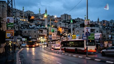 A city street at dusk with buses, election posters, and illuminated mosque minarets in the background