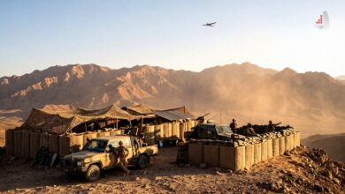 Military soldiers and pickup trucks stationed at a sandbagged outpost in a mountainous desert region