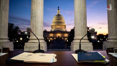 Microphones and folders on a wooden desk facing the US Capitol building