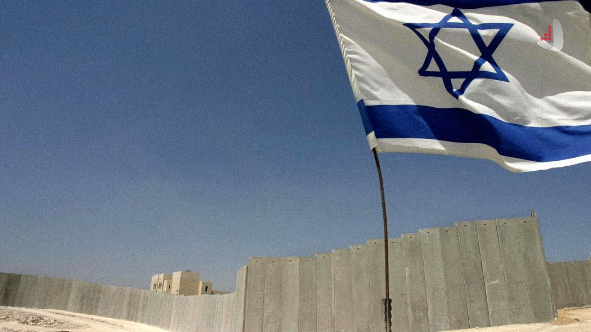 Raised Israeli flag standing in front of a tall concrete separation wall