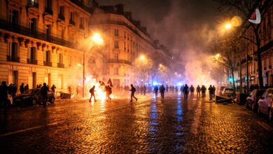 Protesters marching through Paris streets amidst street fires, smoke, and riot police presence
