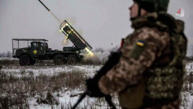 Ukrainian soldier standing in the foreground as a multiple rocket launcher fires in a snowy field